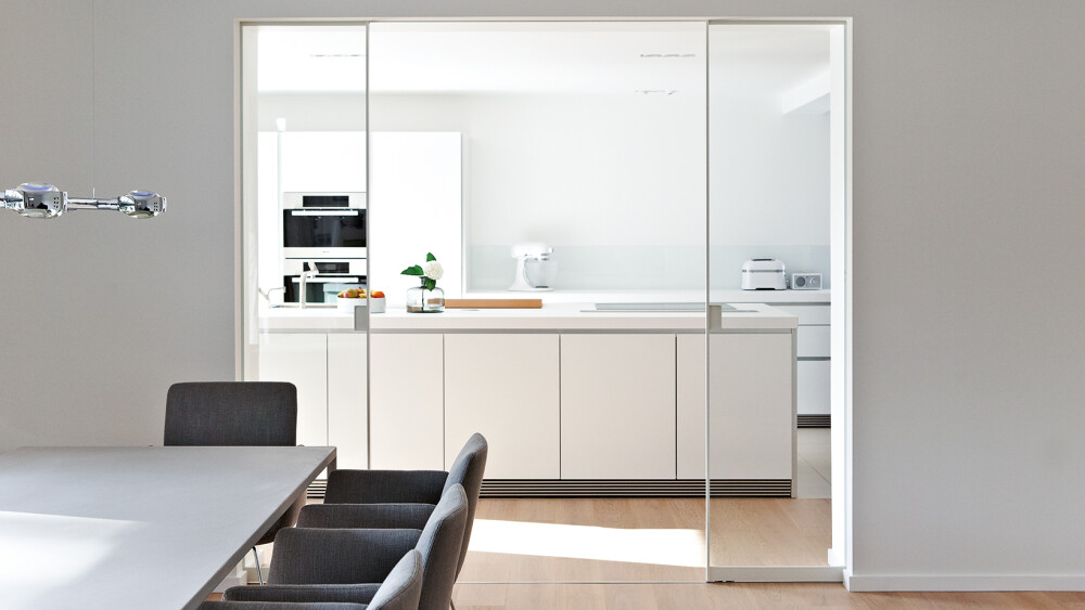 Weiße in einer Wand laufende Alurahmen-Schiebetür mit schmalem Rahmen zwischen Esszimmer und Küche
